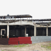 An abandoned building in Iļģuciems with a red and white fence.