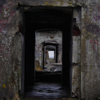 A series of dilapidated doorways creates a haunting tunnel effect in the old, abandoned Karosta building, with layers of graffiti adorning the decaying walls, and nature slowly reclaiming the once