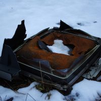 A discarded, rusted television set lies broken on the snowy ground in Karosta, blending decay with the stillness of winter.