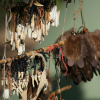 Hanging display of various traditional crafts, including small bone trinkets tied with string and pieces of fur. The items are hung on a wooden pole and feature leather straps, creating a rustic and cultural appearance reminiscent of Kilkim Žaibu festival in 2011. The background is blurred, emphasizing the crafted items.
