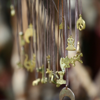 Close-up of several small, brass-colored charms hanging from brown cords at the 2011 Kilkim Žaibu festival. Shapes include animals, abstract figures, and other symbolic designs. The background is blurred, giving a soft focus to the image and placing emphasis on the details and textures of the charms.