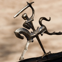 A bronze sculpture depicts an abstract knight on horseback, raising a sword overhead. The minimalist design captures motion and energy, with fluid, exaggerated forms. Set against a softly blurred background, the dynamic and expressive figure channels the spirit of the Kilkim Žaibu festival in 2012.