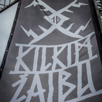 A large black banner with abstract, angular white designs and text hangs between metal scaffolding against a cloudy sky. The stylized text may spell "KILKIM ŽAIBU 2015." The lower right corner of the image has the watermark "xltphoto.net.