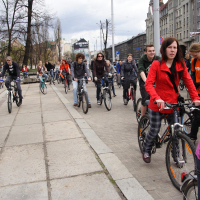 A diverse group of people, some dressed casually and others in sporty attire, ride bicycles on a city street during the 2010 Kritiska masa event. Lined with buildings and marked by trees in the background, the cloudy weather only enhances the scene's active and communal atmosphere.
