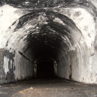 An abandoned, dark tunnel in Liepāja with peeling walls leading into an ominous void, suggesting decay and desolation.