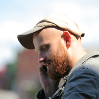 A bearded man in a flat cap is deep in thought, or perhaps conversation, as sunlight highlights his profile against a soft-focus background in Liepāja.