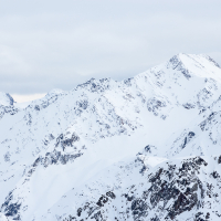 A serene snow-covered mountain range under a cloudy sky, showcasing a mix of shadow and light cascading over the rugged peaks and valleys of Livigno.