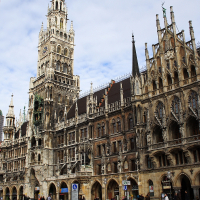 The Gothic Revival architecture of the new town hall graces Munich's Marienplatz, under a clear blue sky, with pedestrians and cyclists enjoying the spacious square.