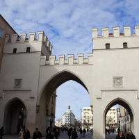 An archway in Munich leads into a bustling square where pedestrians walk under a clear blue sky.