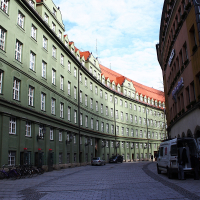 A narrow Munich alleyway with cobblestone streets flanked by green and beige traditional buildings, a parked van on the right, and bicycles lined against the wall under clear skies.