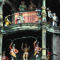 Clock tower in Munich featuring finely crafted, colorful mechanical figurines, possibly depicting historical or folkloric scenes, encased behind protective netting, showcasing traditional attire and poised mid-motion to simulate a performance
