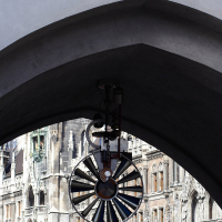 An antique bicycle hangs beneath an arched stone entryway emblazoned with "spielzeugmuseum," with the ornate facade of the new town hall in Munich, Germany, visible in the