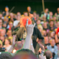 A large crowd at a punk concert, with a hand in the foreground making the "rock on" gesture. The audience is blurred in the background, and many are cheering or holding up their hands. The atmosphere is lively and energetic, reminiscent of a modern Laulupidu festival.