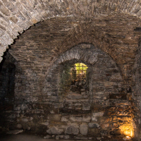 An ancient stone chamber on Saaremaa Island with arched ceilings, illuminated by warm light, leading to a gated entrance that hints at the mysteries of a bygone era.