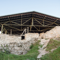 An ancient stone structure in Saaremaa with a modern protective wooden roof, set against a dusk sky, showcasing historical preservation efforts.