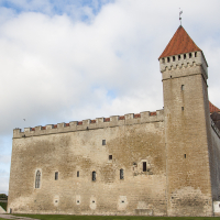 An imposing medieval stone fortress with a sturdy red-tiled tower on Saaremaa Island, standing under a cloud-speckled blue sky, evokes centuries-old tales of knights and nobility.