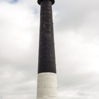 A tall, cylindrical lighthouse on Saaremaa Island, Estonia, with a stark black and white design stands sentinel against a cloudy sky, its beacon poised to guide mariners safely through coastal waters