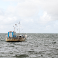 A solitary fishing boat with a blue cabin floats on choppy sea waters near Saaremaa, evoking a sense of calm isolation amidst the vastness of the ocean.