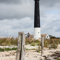 A towering black and white lighthouse on Saaremaa Island stands sentinel on a rugged coastline, flanked by weathered wooden posts under a dramatic sky, symbolizing a guiding light for seaf
