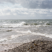 A dynamic seaside scene on Saaremaa Island, with foamy waves crashing onto a pebble beach under a cloudy sky, capturing the raw power of nature.