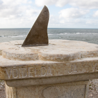 A marble sundial, engraved with "voelda ja vont" and exposed to the elements, overlooks a tranquil sea under partly cloudy skies on Saaremaa Island, Estonia.
