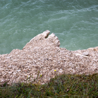 A jagged limestone outcrop extends into the emerald waters below, contrasting with the soft green grasses at the edge of a serene lake in Saaremaa.
