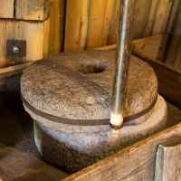 An antique manual grain mill made of stone, with a wooden handle, used for grinding grains into flour, set inside a rustic wooden structure in Saaremaa.