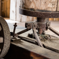 An antique wooden grain millstone set upon a rusted iron support, flanked by weathered gears, embodies a bygone era of manual milling inside a dusty, vintage mill on the island of Sa