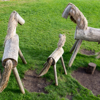 Wooden sculptures resembling horses and a foal, ingeniously crafted from logs and branches on Saaremaa, stand in a green field to mimic equine forms, inviting playful interaction and imaginative outdoor