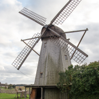 A traditional wooden windmill stands against a cloudy sky on the island of Saaremaa, Estonia, its large sails poised as though ready to catch the wind on a gentle day, with grass and