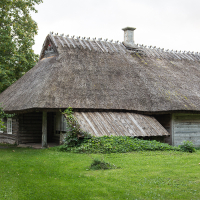 A rustic wooden cottage in Saaremaa with a textured thatched roof, surrounded by lush greenery in a verdant countryside setting, evokes a serene, pastoral atmosphere.