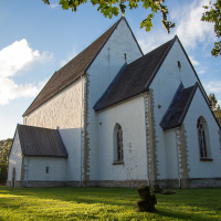 An ancient, white-walled church in Saaremaa basks in the golden light of a setting sun, standing serenely amid lush greenery, its gothic windows whispering tales of