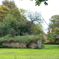A quaint, rustic scene on the Estonian island of Saaremaa, with traditional stone and thatched-roof structures, lush greenery, and trees showcasing rural heritage.