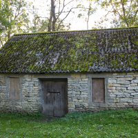 An old stone cottage on Saaremaa, with a moss-covered roof surrounded by lush greenery, evokes a sense of rustic charm and history.