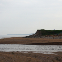 A tranquil beach scene in Scotland with a meandering stream flowing into the sea, under a cloudy sky, as people enjoy a peaceful stroll along the shore with verdant headland in the background.
