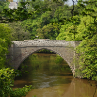 A serene view of an old stone arch bridge crossing a tranquil river in Scotland evokes a sense of peace, history, and the beauty of Scottish culture.