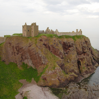 A picturesque ruin of a medieval castle perched atop a rugged coastal cliff in Scotland, under a cloudy sky, overlooking the sea.
