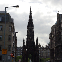 An ornate gothic spire, the Scott Monument, dominates the skyline on a cloudy day amidst Edinburgh's urban streetscape, exemplifying Scotland's historical architecture and Scottish culture.