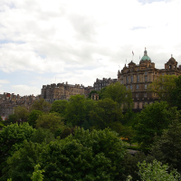 A panoramic view of Edinburgh's historic skyline with lush greenery in the foreground, featuring traditional sandstone buildings and the iconic copper dome of the Bank of Scotland headquarters under a cloudy sky, embodies the essence