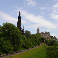 Lush green park with people relaxing under the shade, leading up to the historical Scott Monument with Edinburgh's cityscape in the background under a clear blue sky, showcasing the beauty of Scotland tourism.