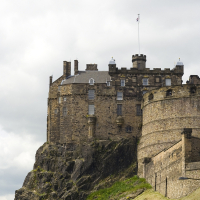 Historic Edinburgh castle perched on an extinct volcanic crag, under a partially cloudy sky, flaunting Scotland's rugged beauty and architectural heritage.