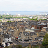 A panoramic view of Edinburgh, showcasing its historic buildings and bustling streets, with the Firth of Forth in the distance under a partly cloudy sky, serves as a testament to Scotland's rich history.