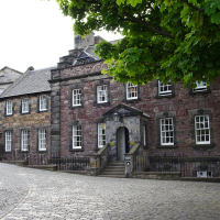 Traditional stone buildings with slate roofs along a cobblestone street in Scotland, with a vibrant green tree adding a touch of nature to this historic urban scene.
