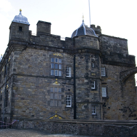 A historic stone castle with turrets and a partially ruined wall under a clear sky in Scotland, showcasing a blend of architectural styles and periods, likely a site of historical significance for tourism.
