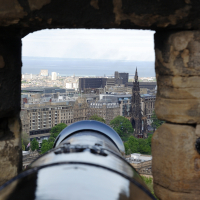 Historic cannon overlooking Edinburgh with the Scott Monument and cityscape, framed by the stone walls of Edinburgh Castle, offering insights into Scottish culture.