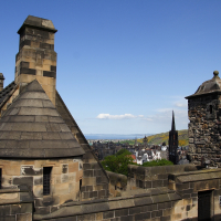 A sunny day at Edinburgh Castle during a Scotland visit, showcasing its historic stone architecture with the city sprawled in the distance, under a clear blue sky.