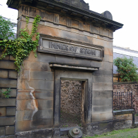 An old stone mausoleum in Scotland with the inscription "innes of stow" adorned by creeping ivy, showcasing historic architecture with a weathered texture and an adjacent rustic wall.
