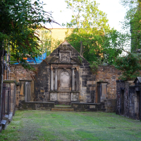 A tranquil graveyard in Scotland at dusk, showcasing an ornate, weathered stone mausoleum surrounded by aged headstones and crypts, nestled within a serene green space flanked by mature trees