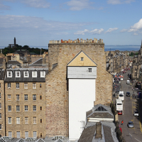 A high-angle view of Edinburgh's historic skyline showcasing traditional sandstone buildings with a clear blue sky, highlighting the city's rich architectural heritage and bustling urban life, an iconic scene for Scotland tourism.