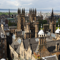 Aerial view of gothic spires and historical stone buildings under a partly cloudy sky in Scotland, showcasing the architectural heritage and urban landscape of an old European city.
